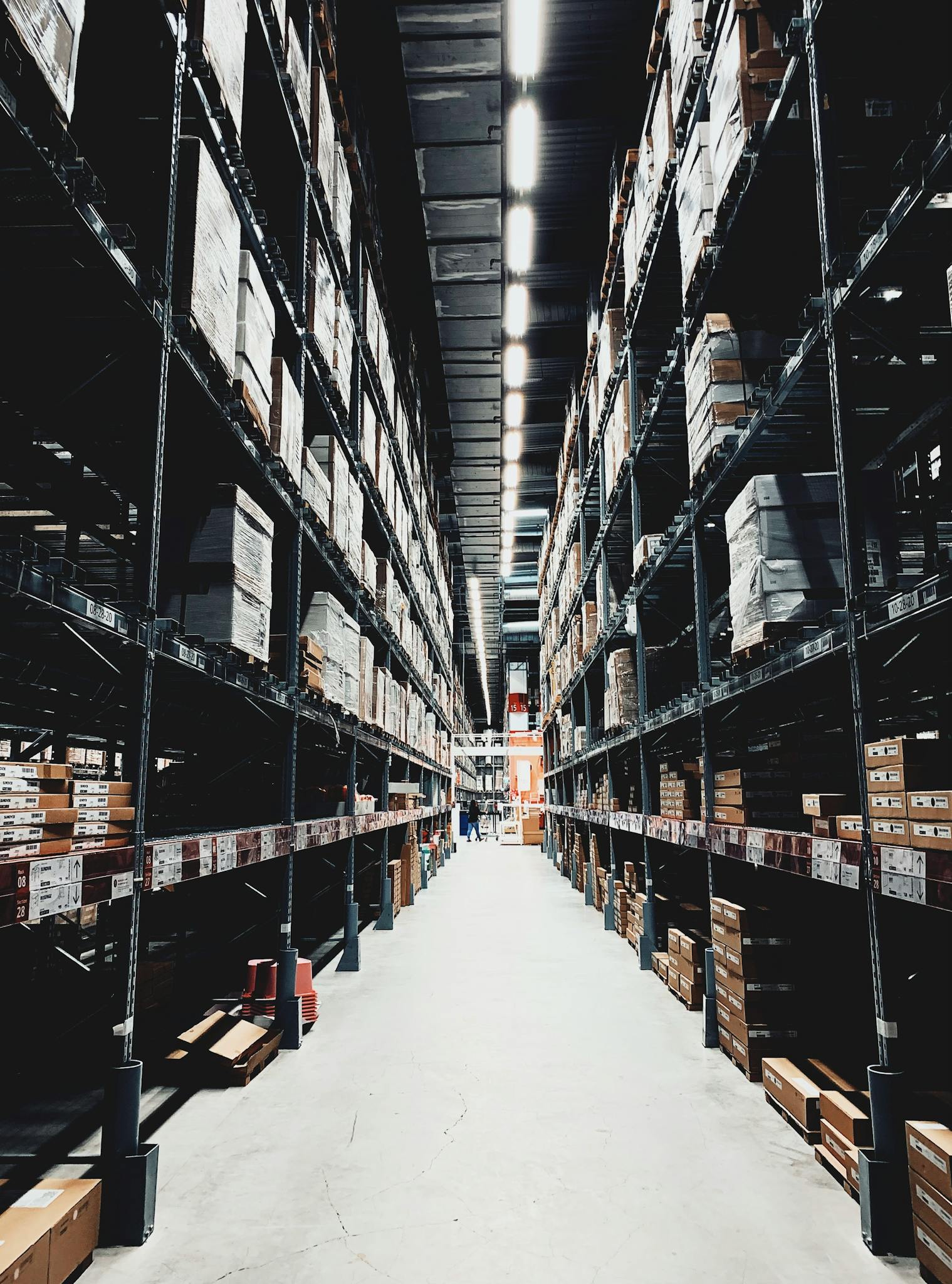 Home A wide aisle in a large warehouse filled with stacked boxes on high shelves.