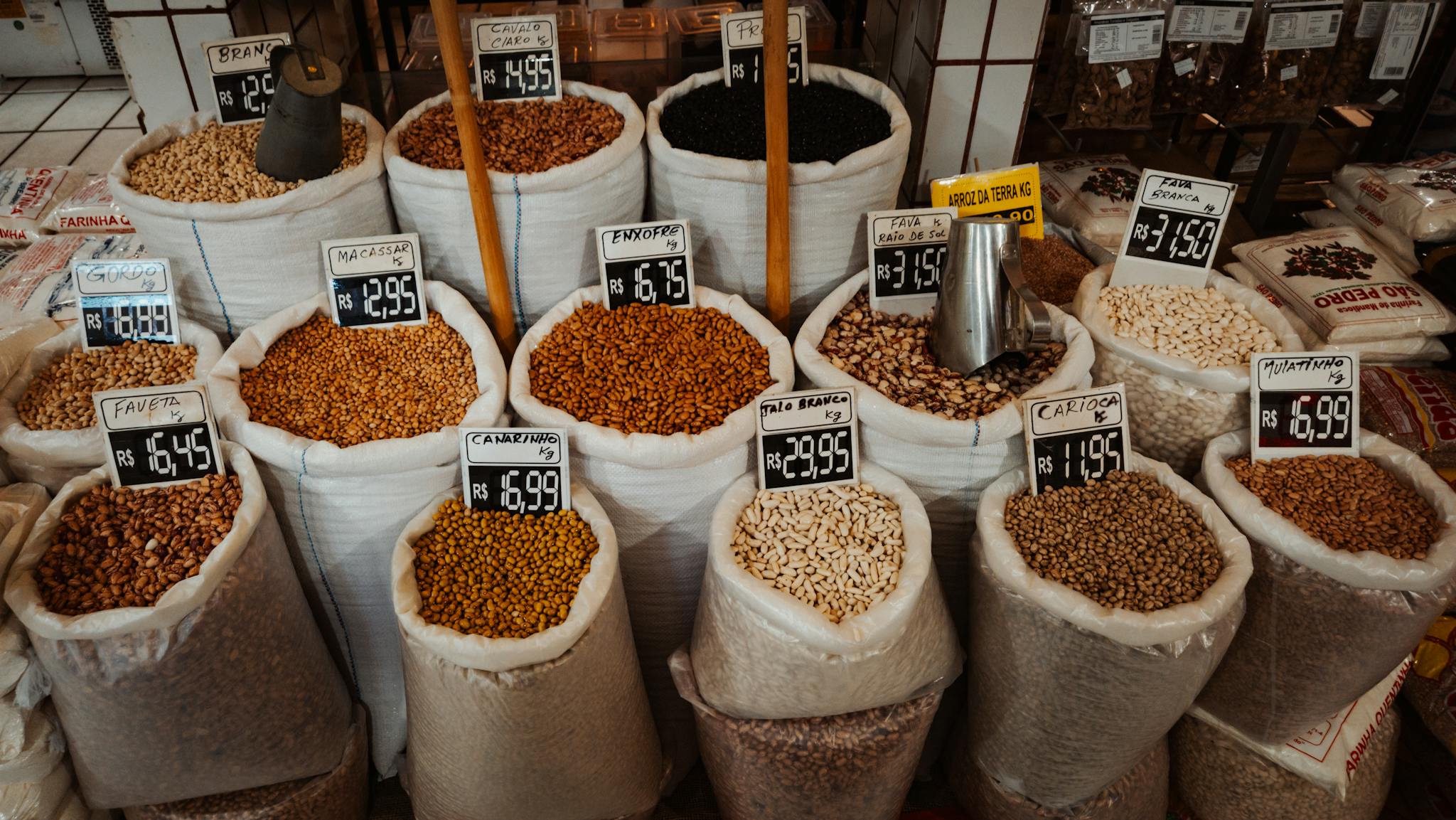 Home Colorful market display of various beans in large sacks with price tags.